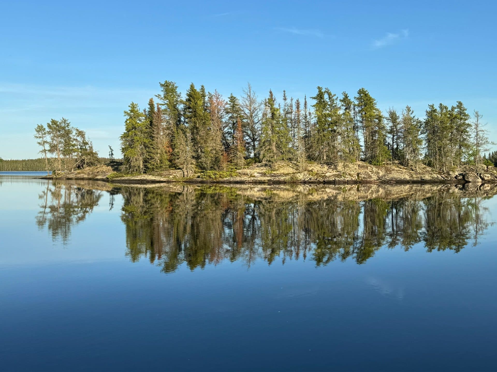Boreal forest island reflected in glass-calm water on Dogskin Lake